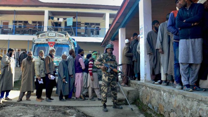 Lok Sabha polls: Phase 3 A security personnel stands guard as voters stand in a queue to cast their votes at a polling station in Anantnag district of Jammu and Kashmir