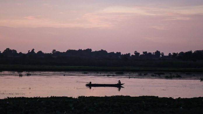 A man sitting on a boat fishes on a river in Cambodia. | Photo: Taylor Weidman | Bloomberg